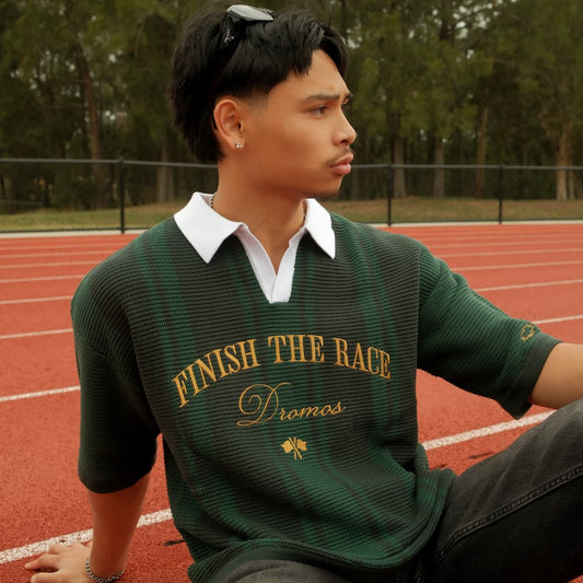 Person wearing a green christian knit polo shirt with text finish the race on a track
