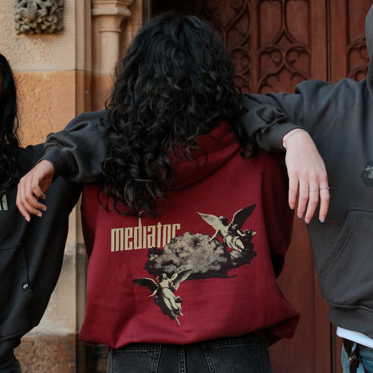 Person wearing a red hoodie with 'mediator' design, standing against a textured wall.