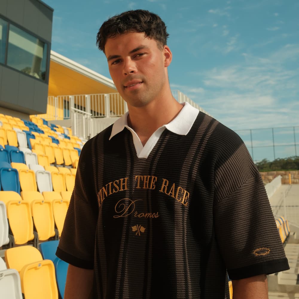 Man wearing a black christian knit polo with text finish the race in an outdoor stadium setting