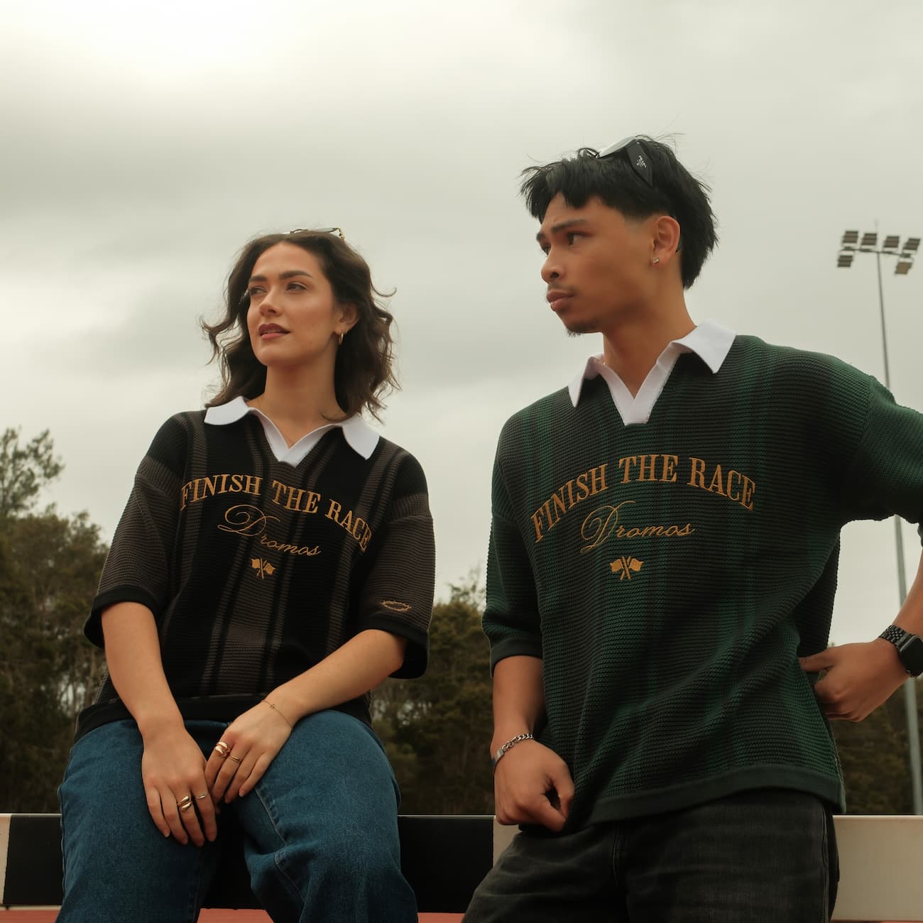 Two people wearing 'Finish The Race' knit polo shirts sitting outdoors on a cloudy day.