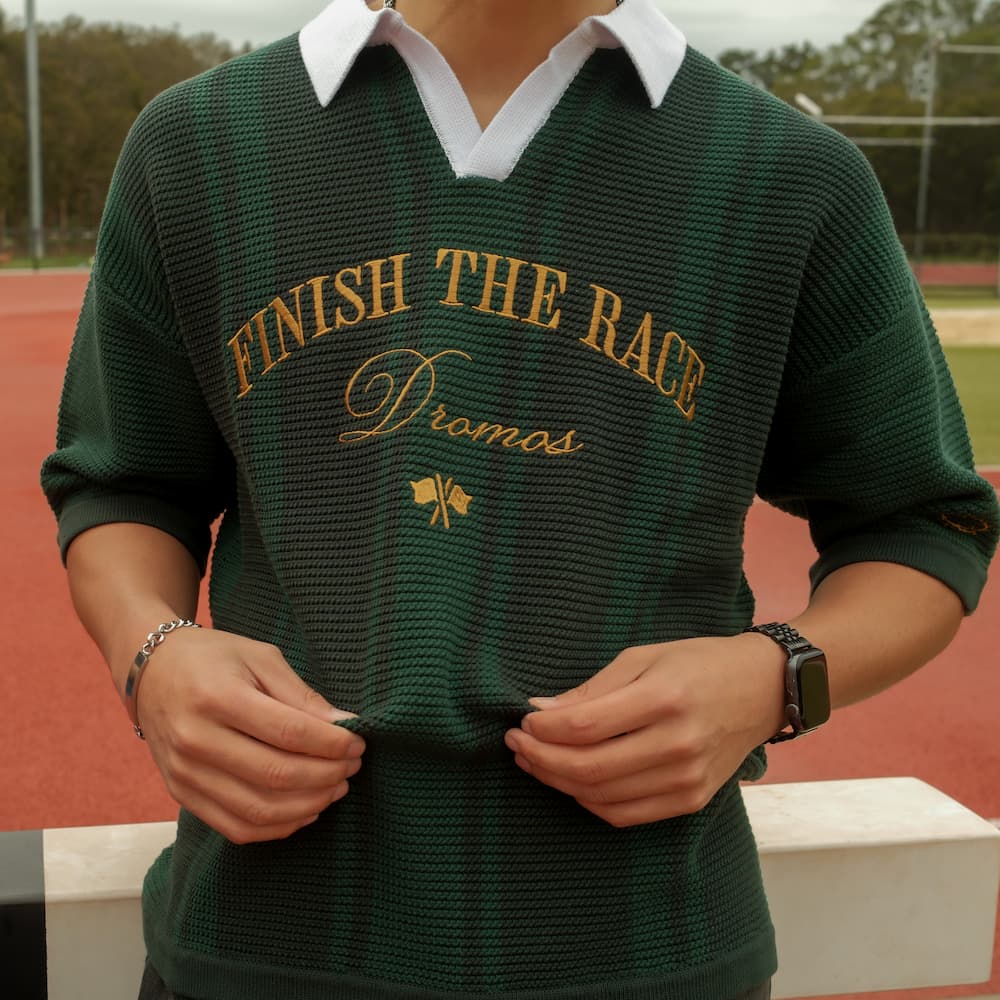 Person wearing a green christian knit polo shirt with text finish the race on a sports field.