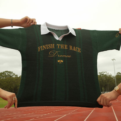 Green knit polo with 'Finish The Race' text held up outdoors on a track.