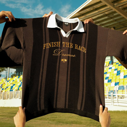 Christina knit polo with text Finish The Race held up in front of a stadium.
