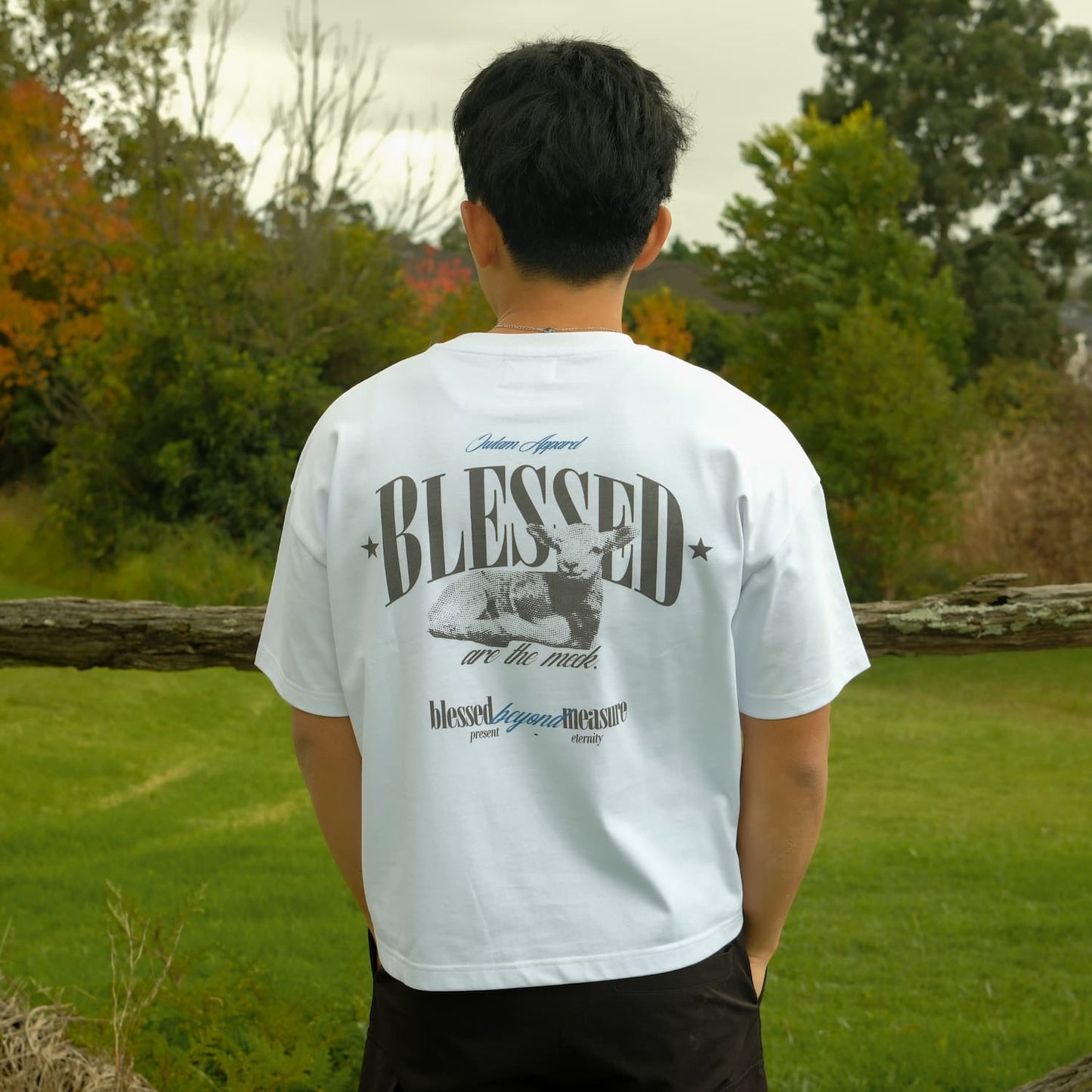 Person wearing a white t-shirt with 'BLESSED' printed on the back, standing outdoors in a natural setting.