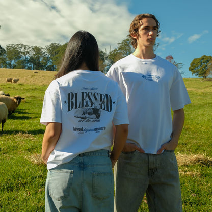 Two people standing in a field with sheep, wearing white t-shirts.