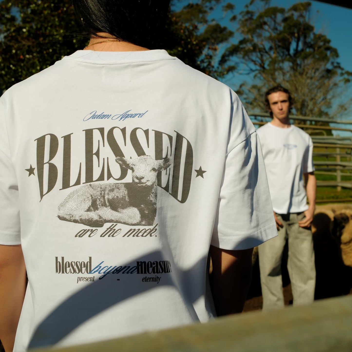 Person wearing a white t-shirt with 'BLESSED' graphic and text, standing outdoors.