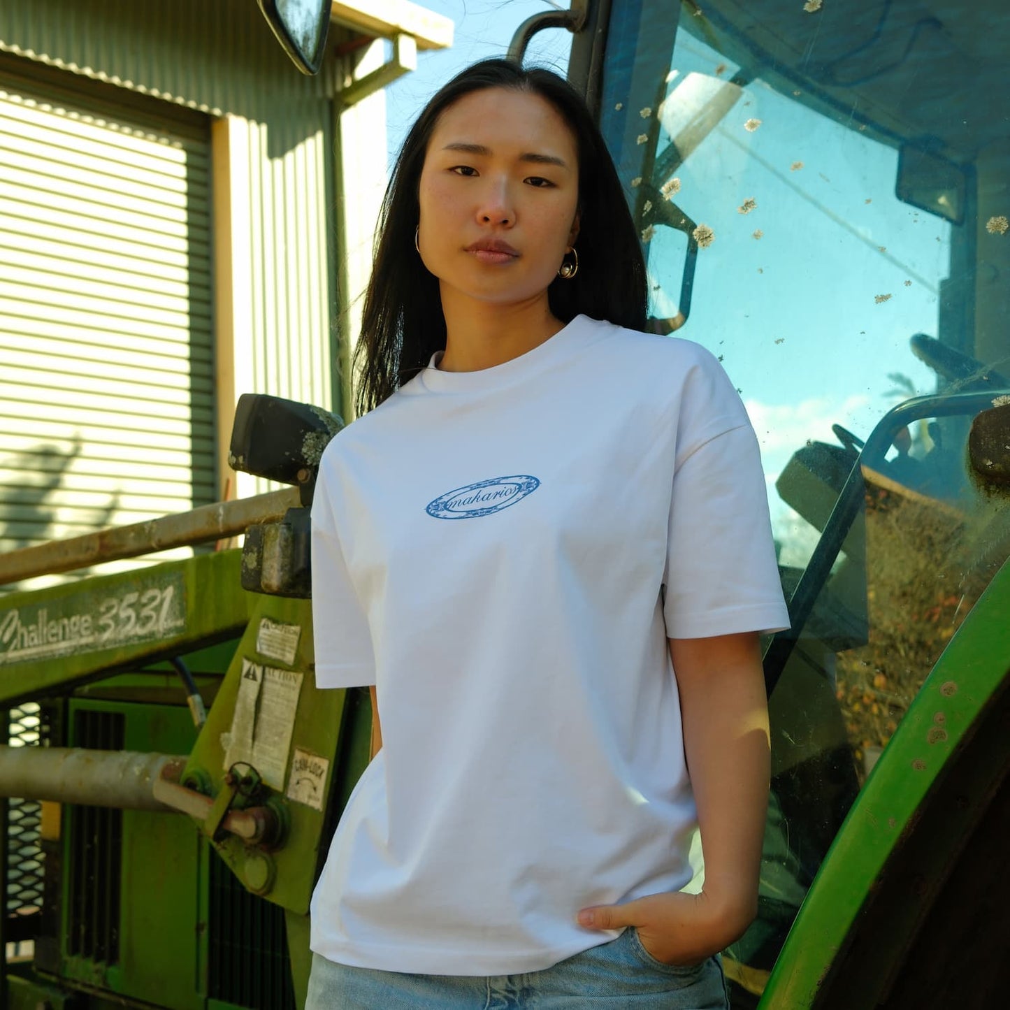 Person wearing a white t-shirt with a logo standing in front of green machinery.