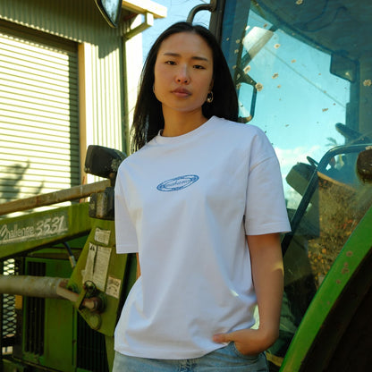 Person wearing a white t-shirt with a logo standing in front of green machinery.